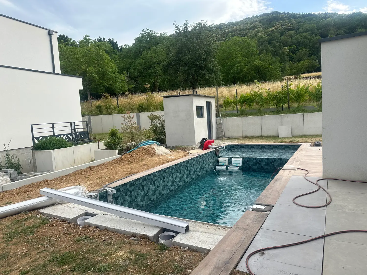 Piscine en cours de remplissage avec liner vert Bali et cabanon en arrière-plan